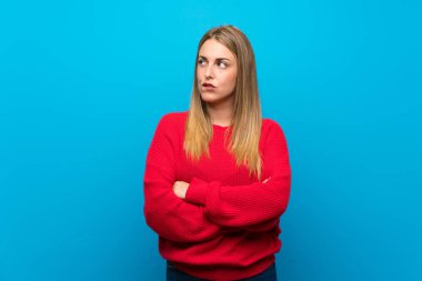 Mavi duvarın üstünde kırmızı kazaklı, kafası karışık bir kadın.