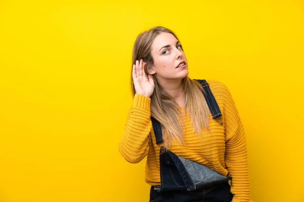 Mujer Con Overoles Sobre Pared Amarilla Aislada Escuchando Algo —  Fotos de Stock