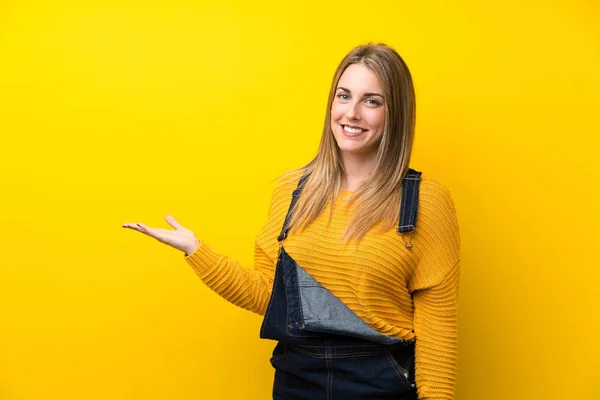Woman Overalls Isolated Yellow Wall Holding Copyspace Imaginary Palm — 스톡 사진