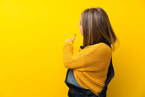 Mujer Con Mono Sobre Pared Amarilla Aislada Apuntando Hacia Atrás —  Fotos de Stock