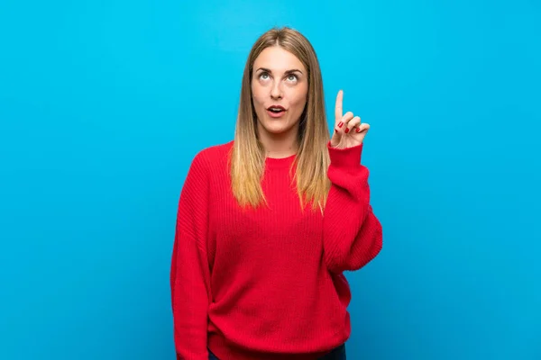 Woman with red sweater over blue wall thinking an idea pointing the finger up