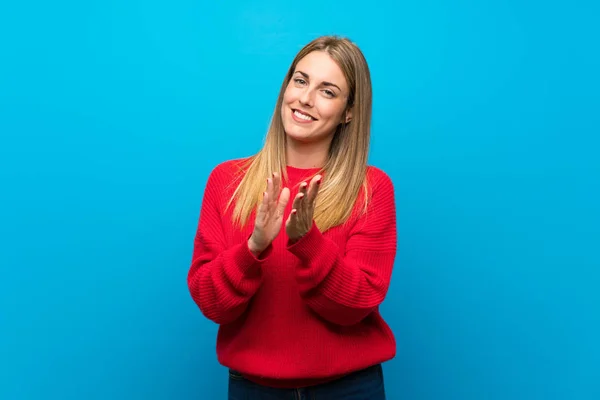 Woman with red sweater over blue wall applauding after presentation in a conference