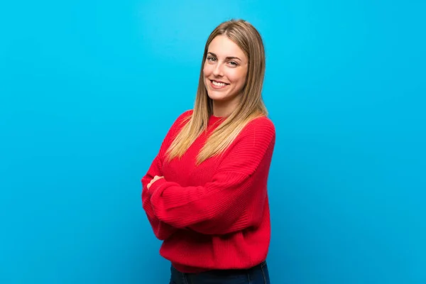 Woman with red sweater over blue wall with arms crossed and looking forward