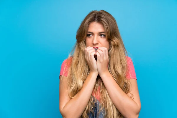 Jovem Loira Com Macacão Sobre Parede Azul Isolada Nervosa Assustada — Fotografia de Stock