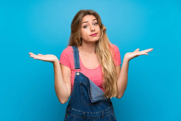 Jeune Femme Blonde Avec Salopettes Sur Mur Bleu Isolé Faisant — Photo