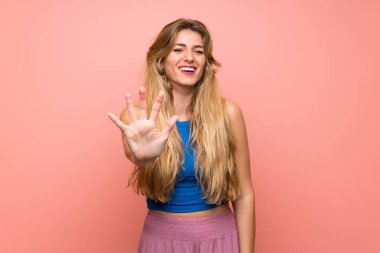 İzole edilmiş pembe arka planı olan genç sarışın kadın parmaklarıyla beşi sayıyor.