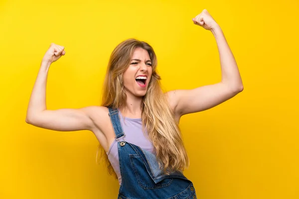 Jovem Loira Com Macacão Sobre Fundo Amarelo Isolado Celebrando Uma — Fotografia de Stock