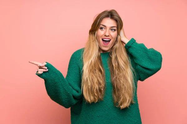 Mujer Rubia Joven Con Suéter Verde Sobre Pared Rosa Sorprendida —  Fotos de Stock