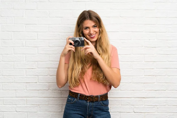 Joven Mujer Rubia Sobre Pared Ladrillo Blanco Sosteniendo Una Cámara — Foto de Stock