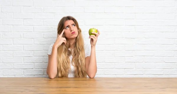 Egy fiatal szőke nő almával, akinek kétségei vannak — Stock Fotó