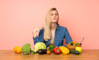 Yorgun ve hasta suratlı, bir sürü sebzeli genç sarışın kadın.