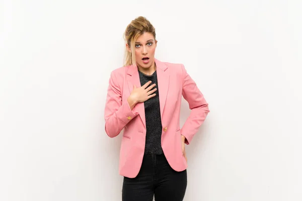 Young blonde woman with pink suit surprised and shocked while looking right