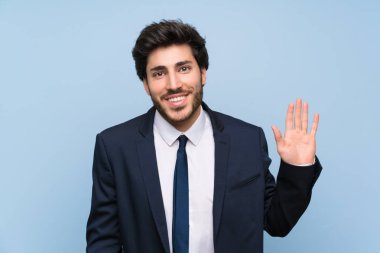 İzole mavi duvar üzerinde mutlu ifade ile el ile selamlama işadamı