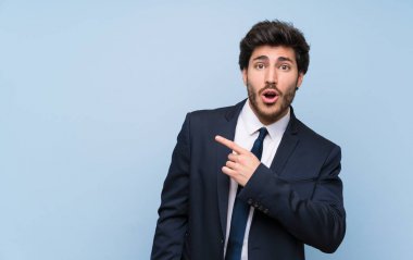 İzole mavi duvar üzerinde işadamı şaşırttı ve yan işaret