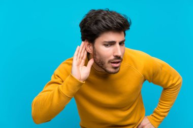 Izole mavi duvar üzerinde yakışıklı kulak elini koyarak bir şey dinlerken