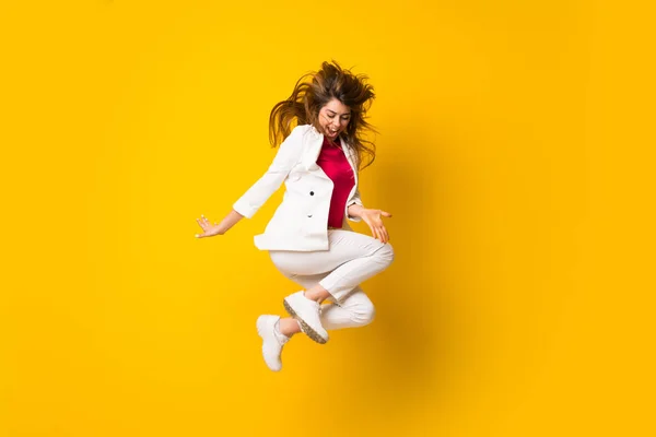 Mujer joven saltando sobre la pared amarilla aislada —  Fotos de Stock