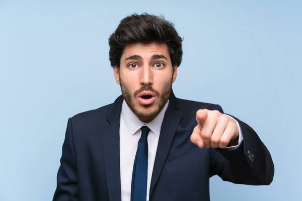 stock image Businessman over isolated blue wall surprised and pointing front