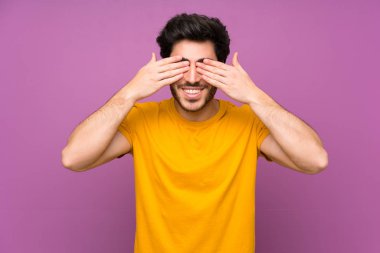 Elleriyle gözleri kaplayan izole mor duvar üzerinde Yakışıklı