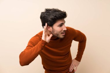 Kulak üzerine el koyarak bir şey dinlerken izole duvar üzerinde Yakışıklı