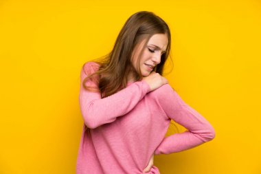 İzole edilmiş sarı duvarın üzerinde uzun saçlı genç bir kadın omuz ağrısından muzdarip.