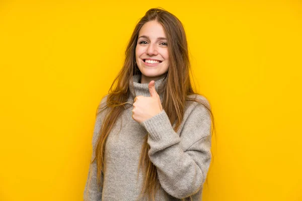 黄色の背景の上に長い髪を持つ若い女性は 親指を上げるジェスチャーを与える — ストック写真