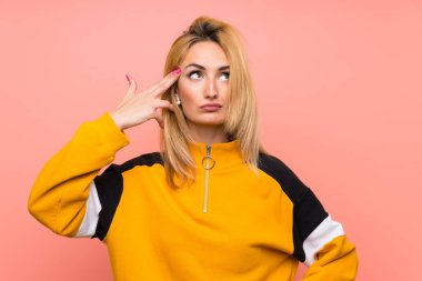 Soyutlanmış pembe arka planı olan genç sarışın kadın intihar jesti yapmada sorun yaşıyor.