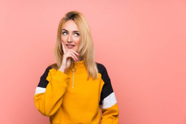 Soyutlanmış pembe arka planı olan genç sarışın kadın yukarı bakarken bir fikir düşünüyor.