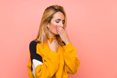 Soyutlanmış pembe arka planı olan genç sarışın kadın öksürük ve kötü hissetmekten muzdarip.