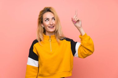 Soyutlanmış pembe arka planı olan genç sarışın kadın parmağını kaldırarak çözümü bulmaya çalışıyor.