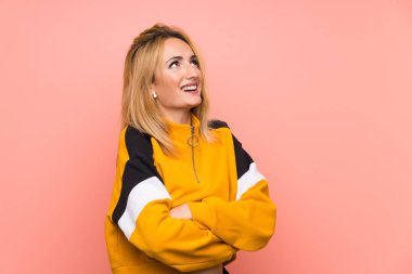 Soyutlanmış pembe arka planda genç sarışın kadın gülümserken yukarı bakıyor.