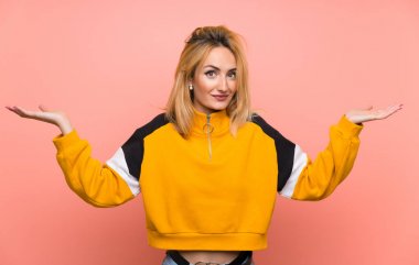 Soyutlanmış pembe arka planı olan genç sarışın kadın ellerini kaldırırken şüphe duyuyor.