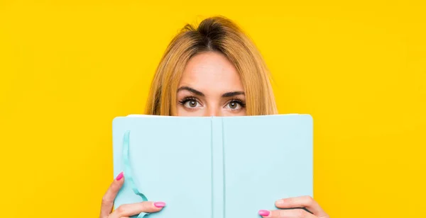 Young Blonde Woman Isolated Yellow Wall Holding Reading Book — Stock Photo, Image