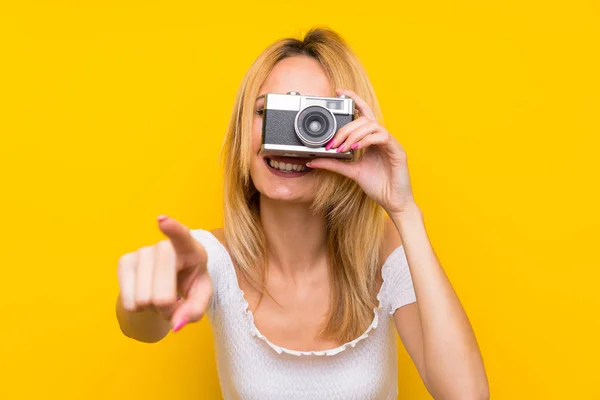 Young Blonde Woman Isolated Yellow Wall Holding Camera — Stock Photo, Image