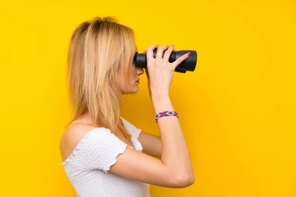 Jovem Loira Sobre Isolado Parede Amarela Com Binóculos Pretos — Fotografia de Stock