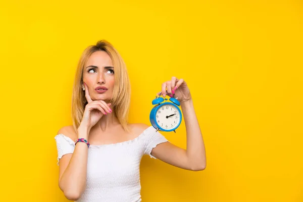 Mujer Rubia Joven Sobre Pared Amarilla Aislada Sosteniendo Reloj Despertador — Foto de Stock