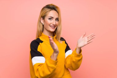 Soyutlanmış pembe arka planı olan genç sarışın kadın bir konferanstan sonra alkışlıyor.