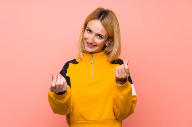 Soyutlanmış pembe arka planı olan genç sarışın kadın para hareketi yapıyor.