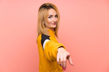 Soyutlanmış pembe arka plandaki genç sarışın kadın kendine güvenen bir ifadeyle seni işaret ediyor.