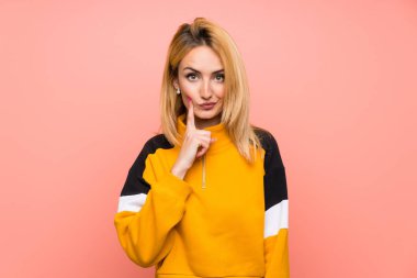 Soyutlanmış pembe arka planı olan genç sarışın kadın önüne bakıyor.