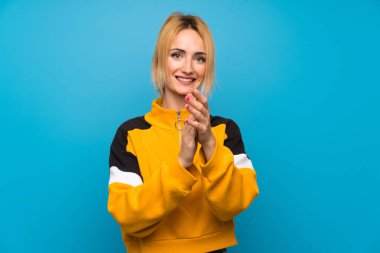 İzole edilmiş mavi arka planı alkışlayan genç sarışın kadın.