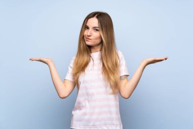 İzole edilmiş mavi arka planı olan genç bir kadın ellerini kaldırırken şüphe duyuyor.