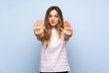 Soyutlanmış mavi arka planda genç bir kadın dur hareketi yapıyor ve hayal kırıklığına uğruyor.