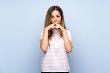 İzole edilmiş mavi arka planda genç bir kadın sessizlik işareti gösteriyor.
