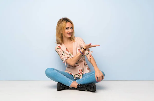 Mujer Rubia Joven Sentada Suelo Presentando Una Idea Mientras Mira —  Fotos de Stock