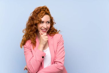 Yan bakan izole mavi duvar üzerinde takım elbiseli Redhead kadın