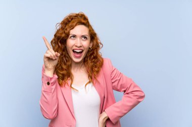 İzole mavi duvar üzerinde takım elbiseli Redhead kadın bir parmak kaldırırken çözüm gerçekleştirmek niyetinde