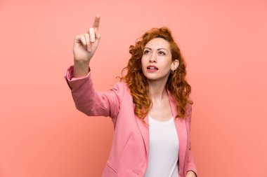 Şeffaf ekrana dokunan izole pembe duvar üzerinde takım elbiseli redhead kadın