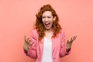 Izole pembe duvar üzerinde takım elbise redhead kadın mutsuz ve bir şey ile sinirli