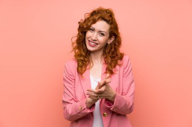 Izole pembe duvar üzerinde takım elbiseli Redhead kadın alkışlıyor