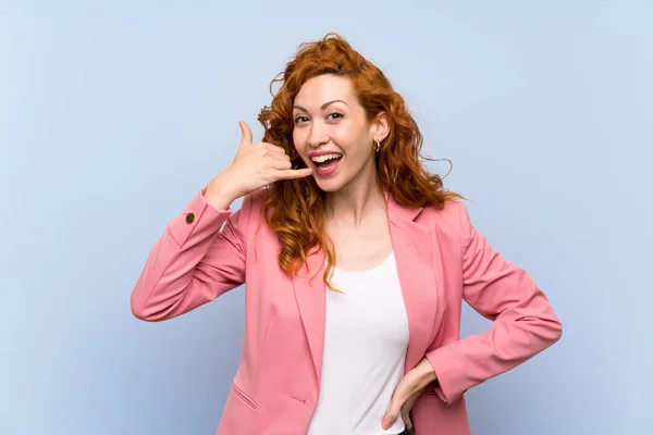 Redhead woman in suit over isolated blue wall making phone gesture. Call me back sign